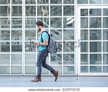 Side view portrait of a male student walking on campus with bag and mobile phone