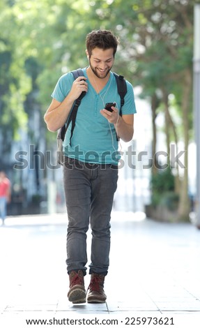 Full length portrait of a smiling man walking in the city with mobile phone and bag