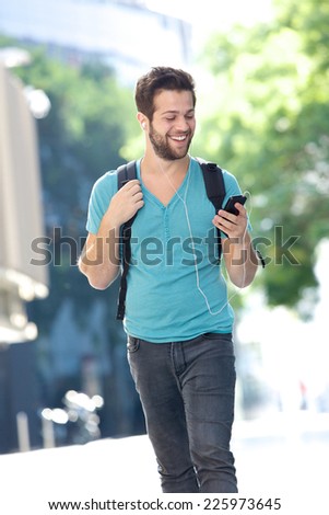 Portrait of a happy male student walking on campus with mobile phone