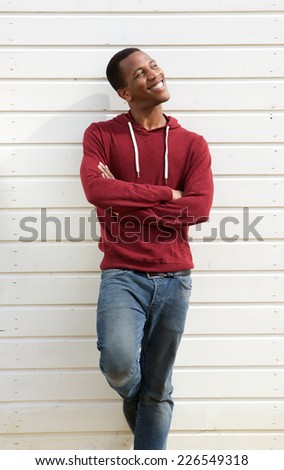 Portrait of a happy young black man standing against white background with arms crossed