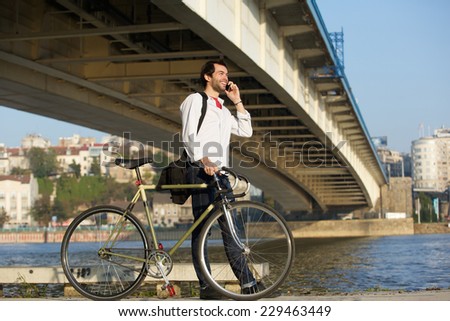 Portrait of a young man walking with bicycle and talking on mobile phone