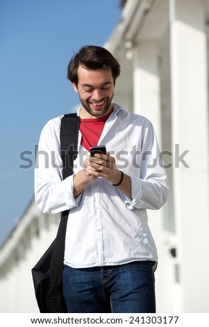 Portrait of a cheerful young man smiling and looking at mobile phone