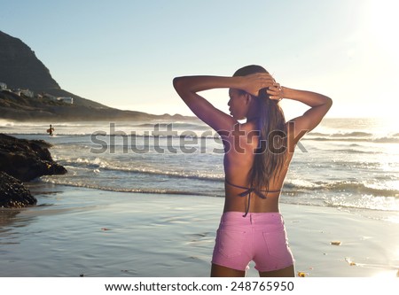 Portrait from behind of a young african woman standing at the beach in bikini