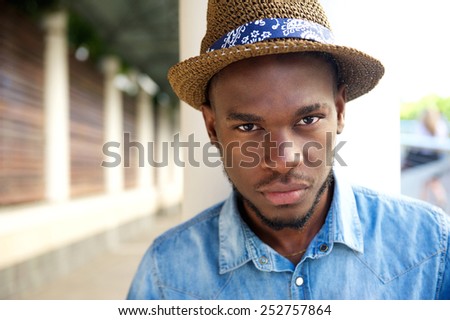 Close up portrait of a cool young african american man posing outdoors with hat
