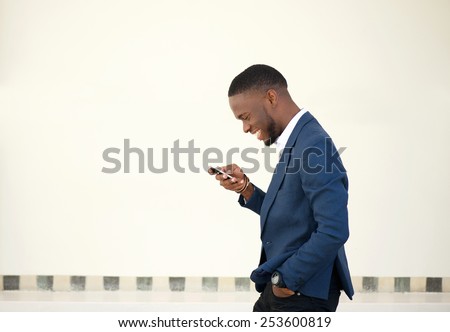 Side portrait of a smiling businessman walking and sending text message on mobile phone