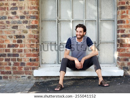 Fresh candid portrait of a happy young man with striped shirt sitting on windowsill