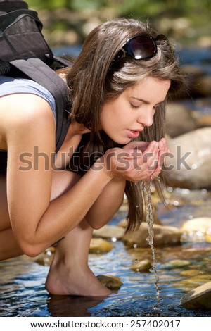 Young female hiker drinking water with hands from outdoor stream