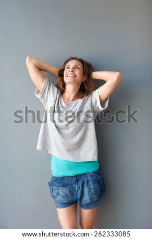 Portrait of a cute mid adult woman smiling with hands behind head against gray background