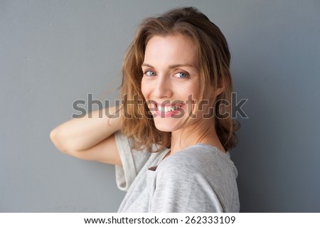 Close up portrait of a happy smiling beautiful woman posing with hand in hair against gray background