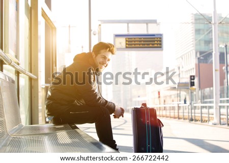 Portrait of a happy young man waiting for train at station with bag