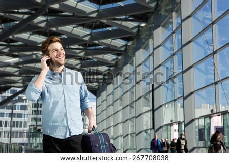 Portrait of a young man smiling at station with bag and mobile phone