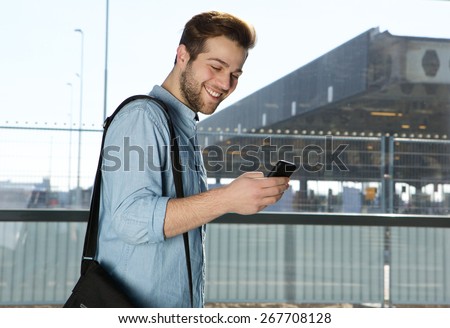 Side portrait of a happy modern man sending text message at airport