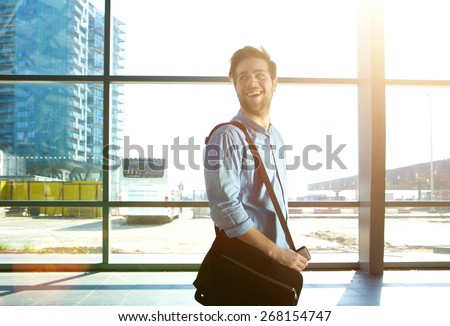 Side portrait of a happy man walking at station with bag
