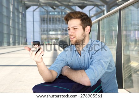 Portrait of a young man looking at mobile phone with confused expression on face