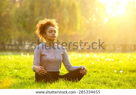 a young African American female is meditating with her eyes closed in nature