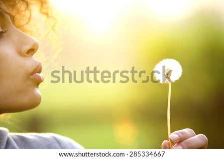 Close up portrait of a young woman blowing dandelion flower outdoors