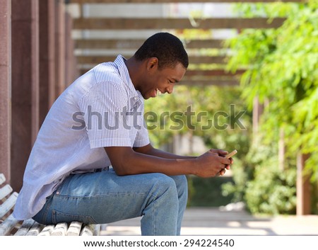Side portrait of a cool african american guy looking at cell phone outside