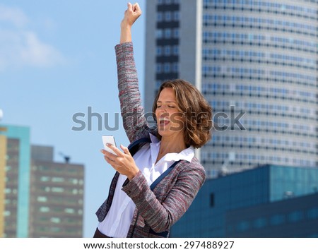 Cheerful business woman reading text on mobile phone and punching the air