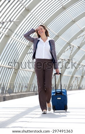 Full body portrait of a business woman smiling and walking at station with bag