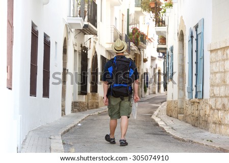 Man walking with backpack and map lost in town - from behind