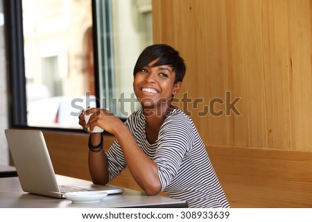 Portrait of a smiling young black woman with coffee and laptop at cafe