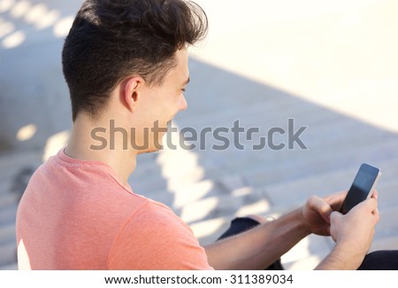 Side portrait of a young guy typing text message on cell phone