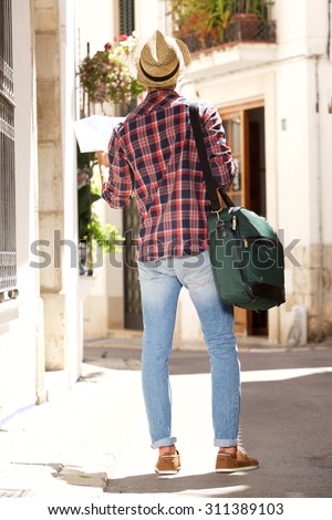 Full body portrait from behind of a traveling man with bag and map