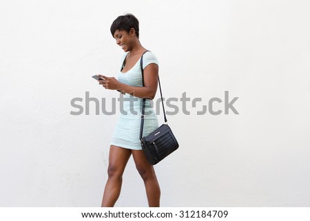 Side portrait of an attractive african american woman walking and looking at cell phone