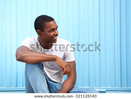 Portrait of a smiling young man sitting against blue wall looking away