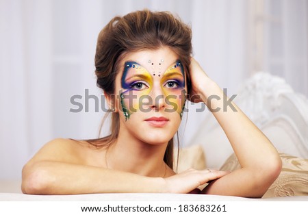 Portrait of beautiful girl with body art butterfly on her face sitting on the couch