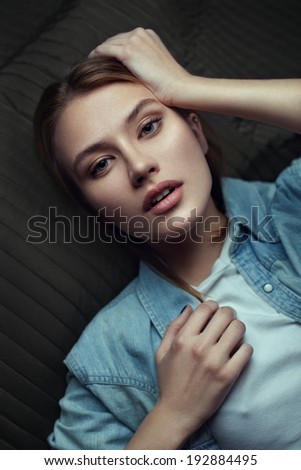 Beauty portrait of a young model in a denim shirt posing lying on back. Red hair. Beautiful girl touching her head.