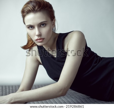 Fashion beauty portrait of young red-haired model with long straight hair in black dress.