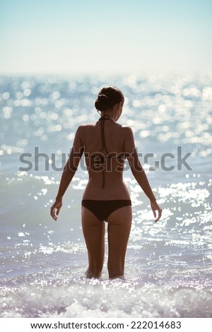 Fashion shot of young beautiful brunette girl in black bikini standing on the beach.