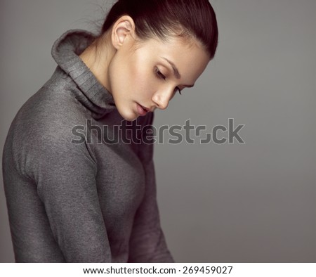 Fashion studio portrait of a young sensual brunette model in gray roll neck jumper. Looking down.