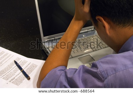Work Stress - A man under pressure at work hangs his head down in despair over his computer.  Shallow depth-of-field : only face is in focus.