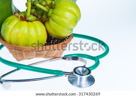 Close up garcinia atroviridis fresh fruit on wood basket and stethoscope on white background. Thai herb and sour flavor lots of vitamin C and good for health. Extract as a weight loss product.