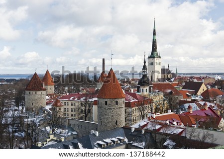 historic Old Town of Tallinn, capital of Estonia. Roofs are covered with snow. Church St. Olaf (Oleviste) at background, curtain wall with towers in foreground.