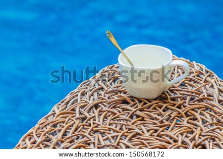 Coffee cup on rattan wicker chair near the pool