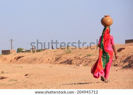 KHICHAN, INDIA - FEBRUARY 12: An unidentified woman carries jar with water on her head on February 12, 2011 in Khichan, India. Village of Khichan is famous for feeding flocks of wintering crains.