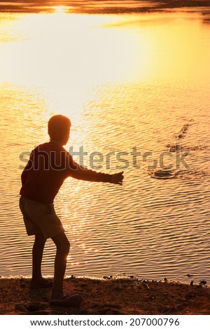 Silhouette of a boy throwing stones in a water, Khichan village, Rajasthan, India