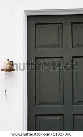 A brass bell hangs next to the green door of a historic building