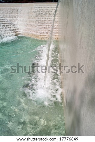 Water flowing down the stairs and over a falls into the cool aqua colored pool of an urban water feature