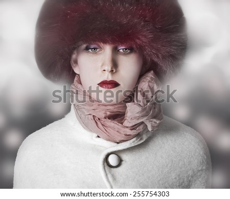 Fashion girl model posing in coat and white furry hat. Winter Beautiful Woman in Luxury clothes over bokeh Christmas Lights background.