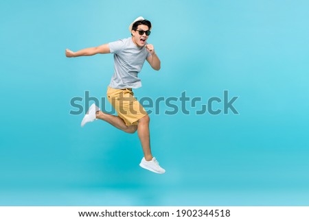 Energetic happy young Asian man jumping studio shot isolated in light blue background