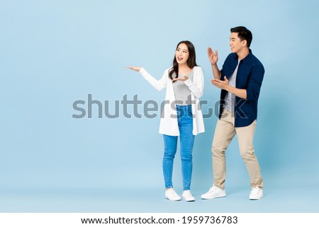 Smiling excited Asian couple tourists pointing hands to empty space aside on isolated light blue background