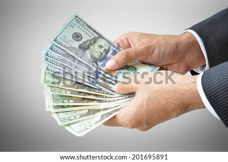 Money - hands holding banknotes (United States Dollars or USD) on gray background
