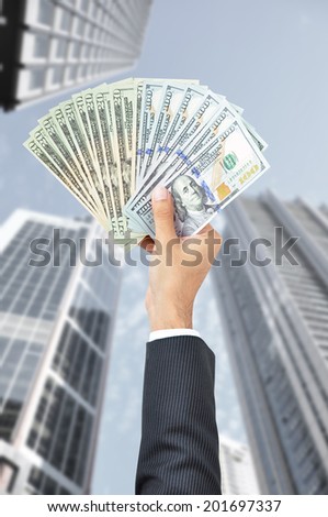 Hand holding money - United States Dollars (or USD) - on building background