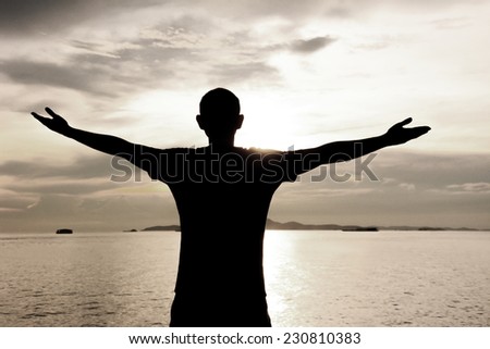Silhouette of a man raising his arms on sea water & sky background - happy, relax & success concept