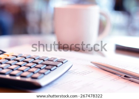 Calculator & pen over paper on the table with blur coffee cup background, coffee break concept - soft focus