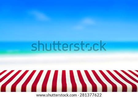 Table covered with striped tablecloth on blurred beach background, picnic and holiday concepts - can be used for display and montage your products